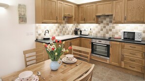 A kitchen with wooden cabinets, a tiled backsplash, a sink, a stove, and a microwave. There is a table with chairs and a vase of flowers. - 1 bedroom accommodation in Wainfleet St. Mary, near Skegness (Wainfleet St. Mary, near Skegness)