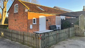A brick house with a white door, a small porch, and a wooden fence. - 1 bedroom accommodation in Wainfleet St. Mary, near Skegness (Wainfleet St. Mary, near Skegness)