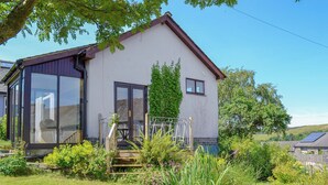 Ein zweigeschossiges Haus mit einem großen Glasbalkon und Fenstern, umgeben von einem Garten mit verschiedenen Pflanzen und einem kleinen Teich.