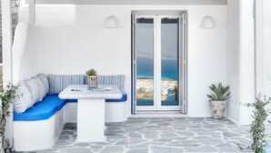 Un espace extérieur aménagé avec des sièges blancs, comprenant une table, un banc bleu avec coussin et un pot de fleurs.