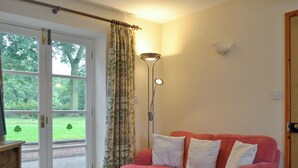 Une pièce avec un canapé rose, un meuble en bois, un lampadaire et une porte donnant sur un jardin.