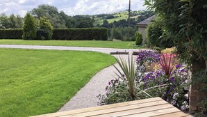 Un banc en bois dans un jardin, avec un chemin de gravier, entouré de verdure et de fleurs.