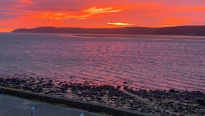 Un paysage de coucher de soleil sur la côte, avec un rivage rocheux et des collines à l'horizon.