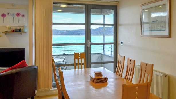 Un coin repas avec une table et des chaises, un canapé, une fenêtre donnant sur la mer et un tableau encadré au mur.