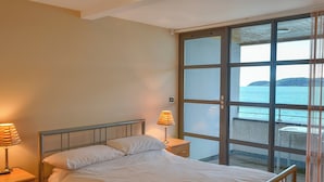 Une chambre à coucher avec un lit, des lampes de chevet, une table de chevet et une grande fenêtre donnant sur la mer.