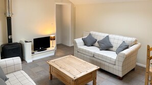 Una sala de estar con sofá, una mesa de centro de madera, televisión, chimenea y lámpara.