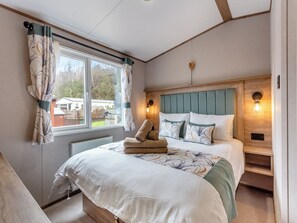 Une chambre à coucher comprenant un lit, des oreillers, une tête de lit, une fenêtre avec des rideaux, un radiateur et un luminaire fixé au mur.