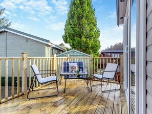 Une terrasse en bois avec deux chaises et une table, une clôture en bois et un grand arbre.