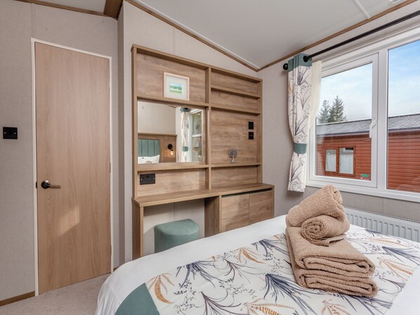 A bedroom with a bed, a desk, a mirror, and a window with a view of a building.