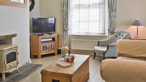 A living room with a television, wooden cabinet, fireplace, and a window with curtains.