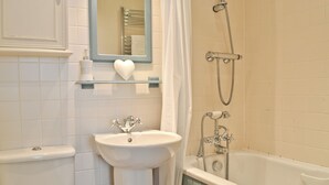 Une salle de bain équipée d’un lavabo, d’un miroir, d’un porte-serviettes, d’une douche et de toilettes.