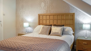 A bedroom with a wooden headboard, a quilted bedspread, two bedside tables with lamps, and patterned wallpaper. - 4 bedroom accommodation in Keswick (Keswick)