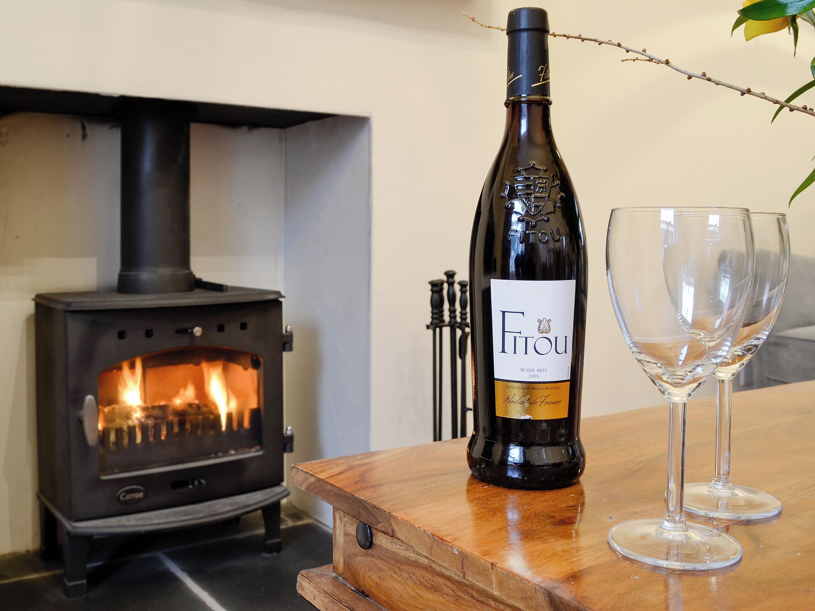 A bottle of Fitou wine, two empty wine glasses, and a wood-burning stove.