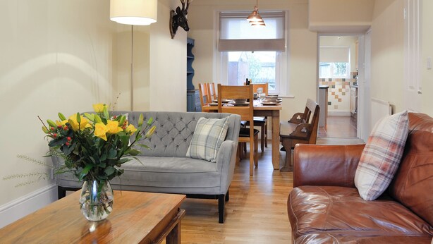 A living room with a sofa, a coffee table, a dining table with chairs, and a kitchen in the background. - 4 bedroom accommodation in Keswick (Keswick)