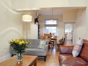 En stue med sofa, sofabord, spisebord med stole og et køkken i baggrunden.
