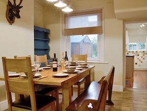 A dining area with a wooden table set for six, chairs, and wine bottles.