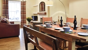 A dining area with a wooden table set for a meal, a television in the background, and a fireplace. - 4 bedroom accommodation in Keswick (Keswick)