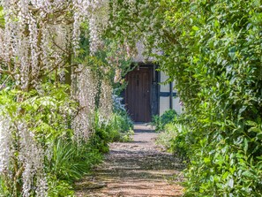 A pathway leading to a wooden door surrounded by lush greenery and white flowers. - 3 bedroom accommodation in Callow End, Worcester (Callow End, Worcester)