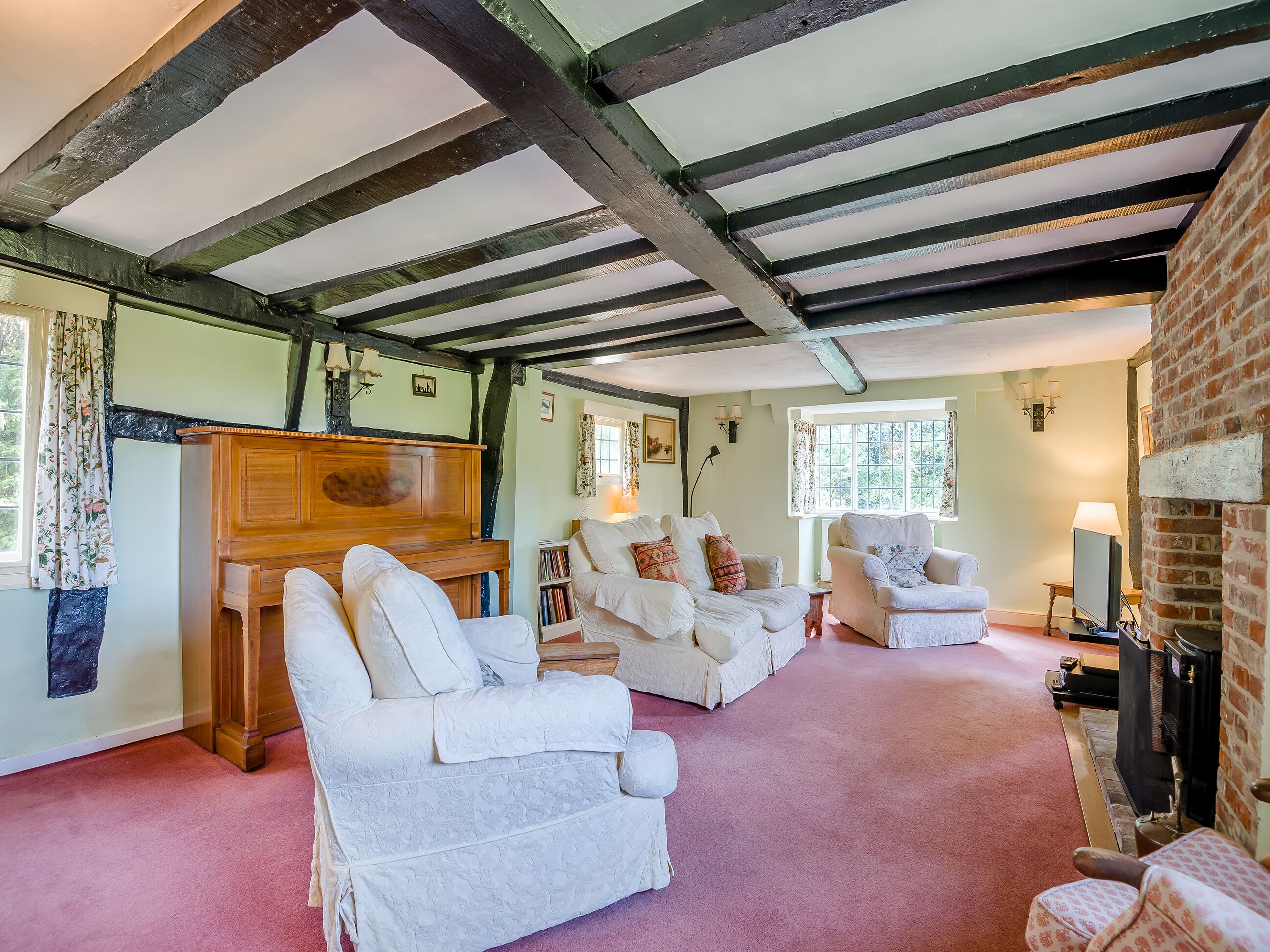 A room with exposed wooden beams, a fireplace, and a cozy seating area with white upholstered furniture.