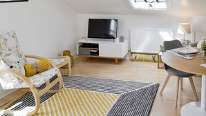 Ein modernes Wohnzimmer mit Fernseher, Sofa, Esstisch und einem Oberlicht.