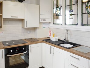 A modern kitchen with white cabinets, a black oven, a stainless steel sink, and a wooden countertop.