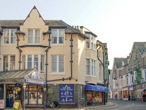 A corner building with a 'Peter Rabbit and Friends' shop, a 'Shopping Centre' sign, and a bicycle parked outside.