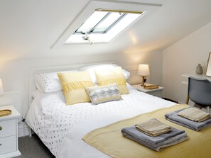 A bedroom with a skylight, a bed with patterned bedding, bedside lamps, a chair, and a small table with a vase.