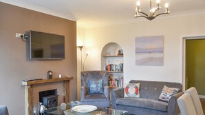 A living room with a fireplace, a sofa, a glass coffee table, and a bookshelf. - 3 bedroom accommodation in Alnmouth, Alnwick (Alnmouth, Alnwick)