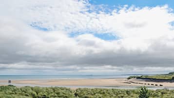 Une plage avec une étendue d’herbe au premier plan et un ciel dégagé.