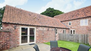 A brick house with a tiled roof, a patio with a table and chairs, and a wooden fence.