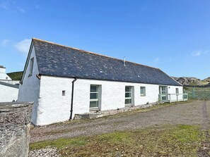 A white building with a slate roof, a gravel driveway, and a stone wall.