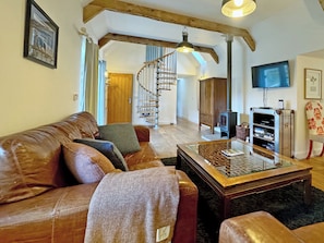 Una sala de estar con un sofá de cuero, una mesa de centro de vidrio, un armario de madera, una televisión y una escalera en espiral.