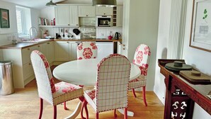 Een keuken met witte kasten, een eettafel met bloemenstoelen en een hangende lamp.