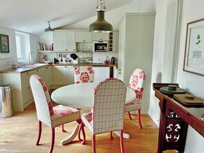 Een keuken met witte kasten, een eettafel met bloemenstoelen en een hangende lamp.