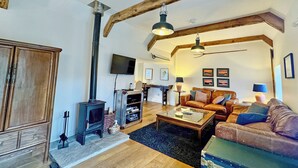 Ein Wohnzimmer mit Kamin, Holzbalken, einer Couch, einem Couchtisch und einem Fernseher.
