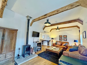 A living room with a fireplace, wooden beams, a sofa, a coffee table, and a television.