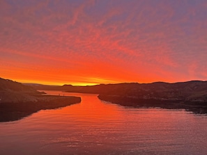 Un atardecer sobre un río tranquilo, flanqueado por colinas.