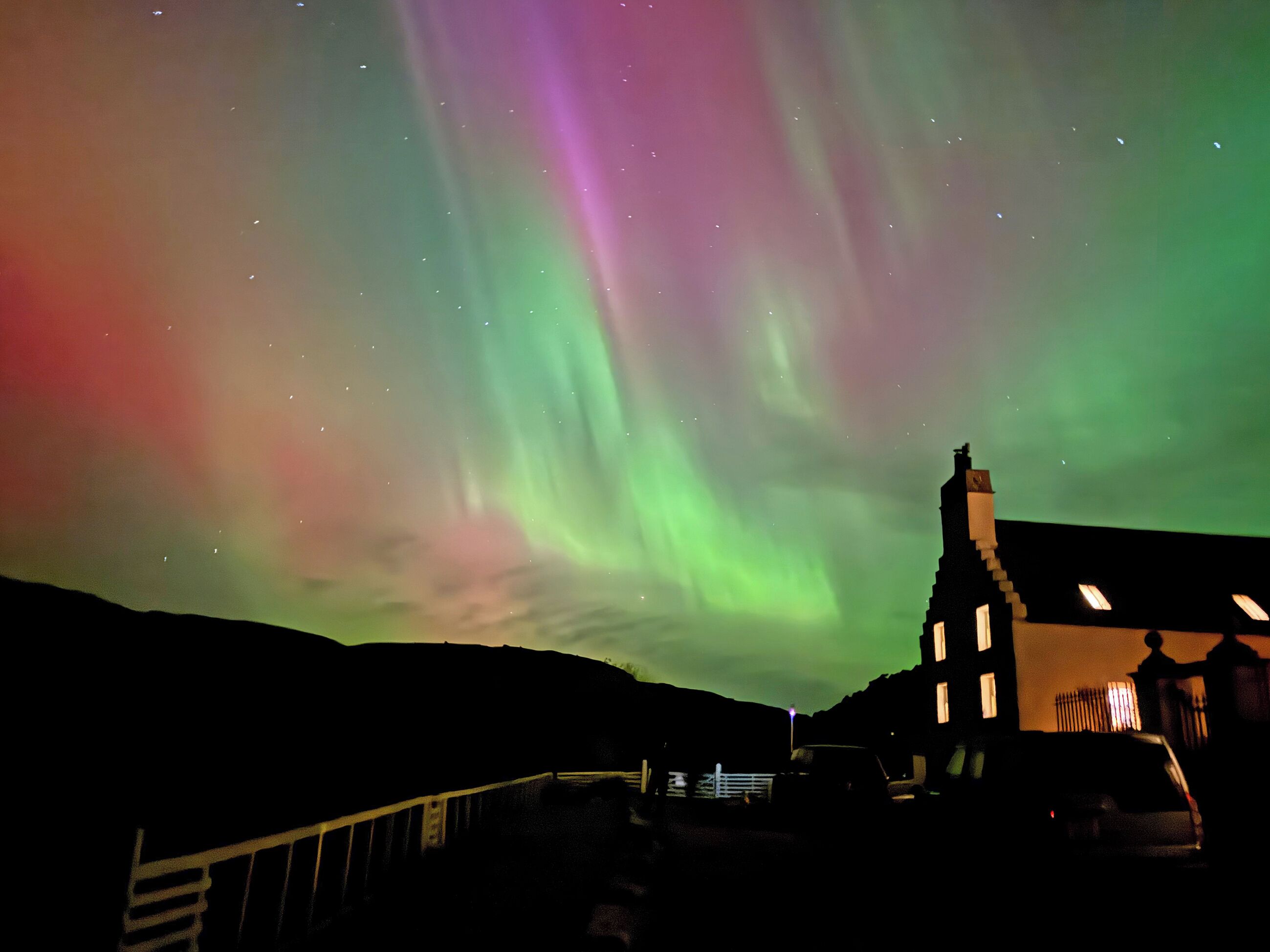 A building with a dark roof and a visible chimney, set against a night sky with the Northern Lights.