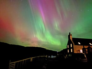 A building with a dark roof and a visible chimney, set against a night sky with the Northern Lights. - 2 bedroom accommodation in Rispond, near Durness (Rispond, near Durness)