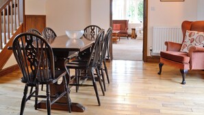 A dining area with a wooden table and chairs, a staircase, and a living room with a sofa and a painting. - 3 bedroom accommodation in Icomb, near Stow-on-the-Wold (Icomb, near Stow-on-the-Wold)