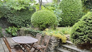 A patio with a round table and four chairs, surrounded by lush greenery and a stone wall. - 3 bedroom accommodation in Icomb, near Stow-on-the-Wold (Icomb, near Stow-on-the-Wold)