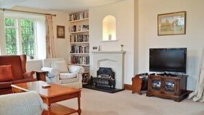 A living room with a fireplace, a bookshelf, a television, and a sofa. - 3 bedroom accommodation in Icomb, near Stow-on-the-Wold (Icomb, near Stow-on-the-Wold)