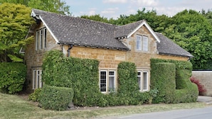 A stone house with a pitched roof, surrounded by well-maintained hedges and trees. - 3 bedroom accommodation in Icomb, near Stow-on-the-Wold (Icomb, near Stow-on-the-Wold)
