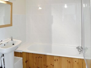 Un bagno con un lavandino bianco, una vasca e rivestimenti in legno.