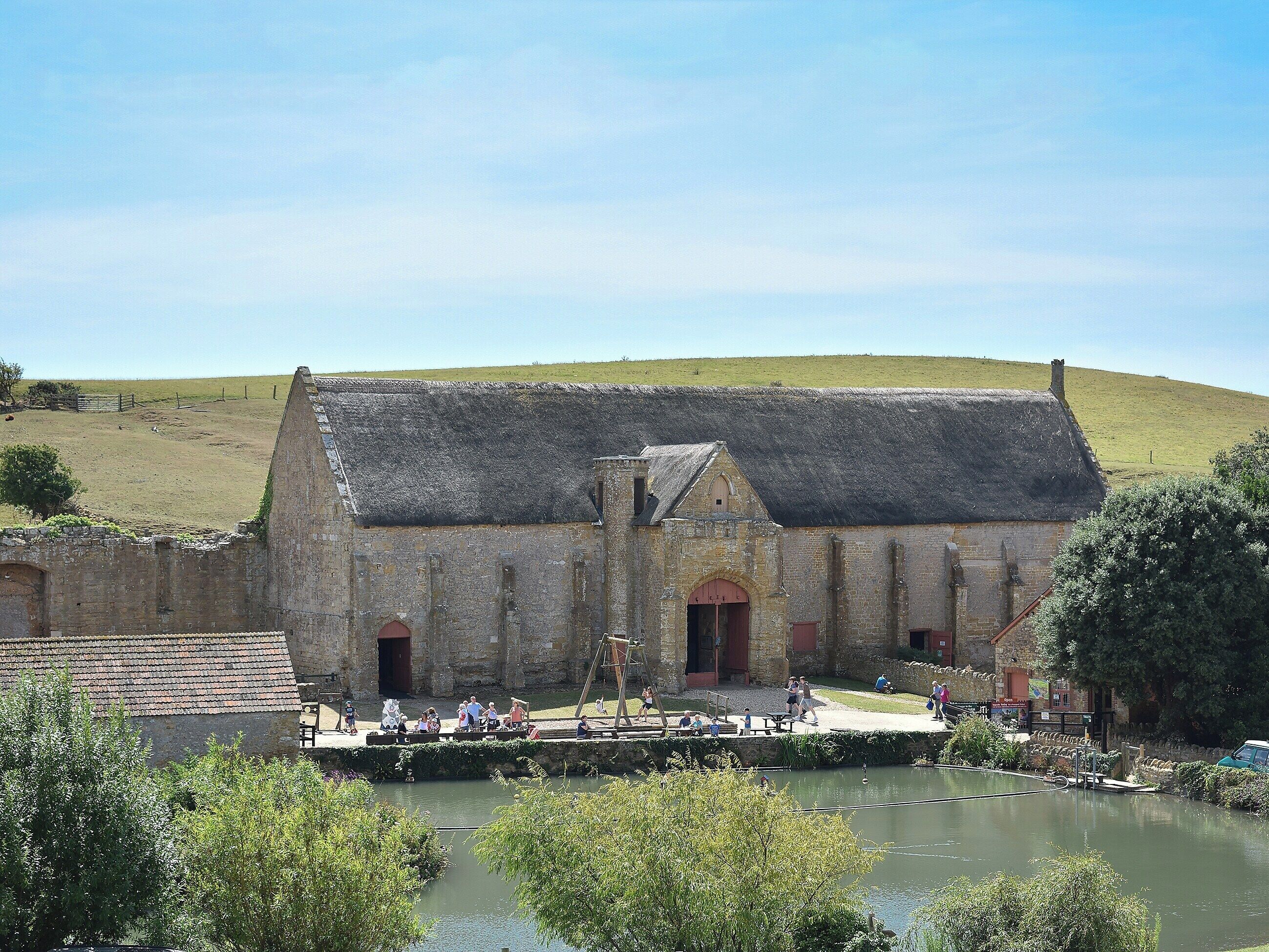 Ein historisches Steinhaus mit einem Strohdach, einem kleinen Innenhof und einem Teich.