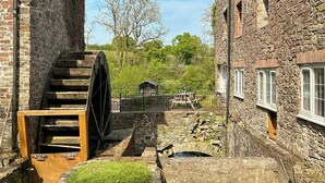 Un edificio histórico de piedra con una noria grande y una estructura de madera pequeña al fondo.