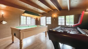Una habitación con mesa de billar, mesa de fútbolín y ventanales con vistas a zonas verdes.
