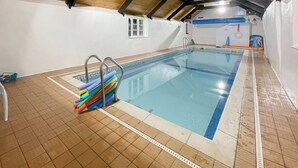 Una piscina interior con suelo de baldosas y techo de madera.