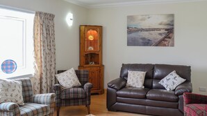 A living room with a brown leather sofa, two plaid armchairs, a wooden cabinet, and a painting on the wall. - 3 bedroom accommodation in Portmahomack, near Tain (Portmahomack, near Tain)