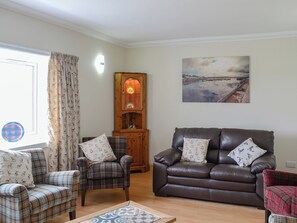 Un salon avec un canapé en cuir marron, deux fauteuils à motifs écossais, un meuble en bois et un tableau accroché au mur.